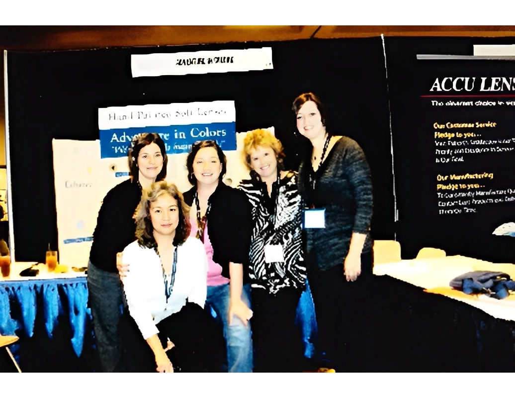 Five people posing together at a booth with banners and a table, displaying products and information.