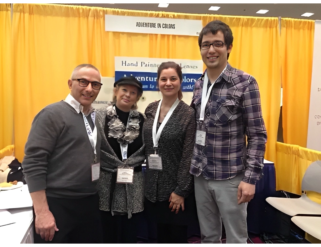Four people wearing conference badges stand smiling in front of a booth with yellow curtains at a convention.
