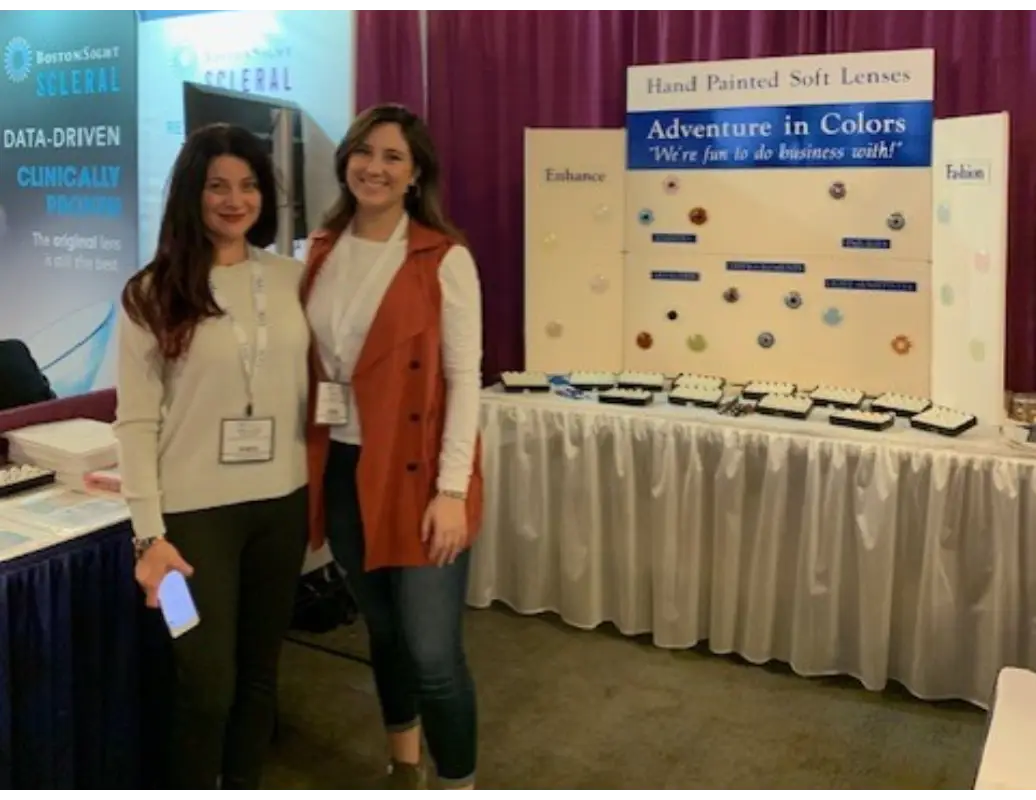 Two women standing in front of a table with a sign.