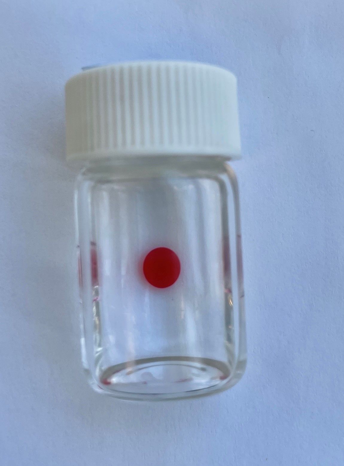 A small glass container with red dot on top.